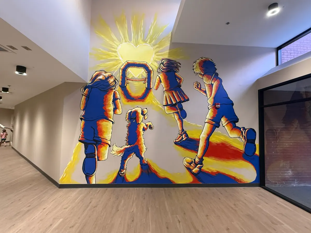 Lovewell 5K mural of kids and a dog running toward a bright sun at Redeemers Structural Solutions.
